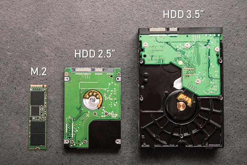 Uma SSD M.2 e duas HDDs dispostas em uma mesa para comparar o tamanho.