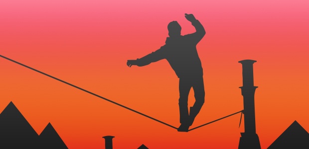 A silhueta de um homem balançando em uma corda bamba contra um céu laranja.